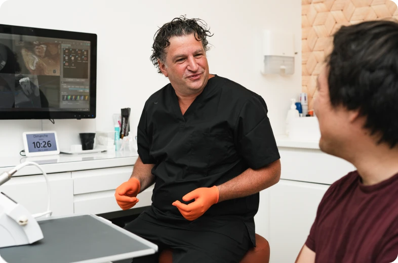 Dentiste en blouse noire discutant avec un patient lors d'une consultation d'endodontie à Paris 16